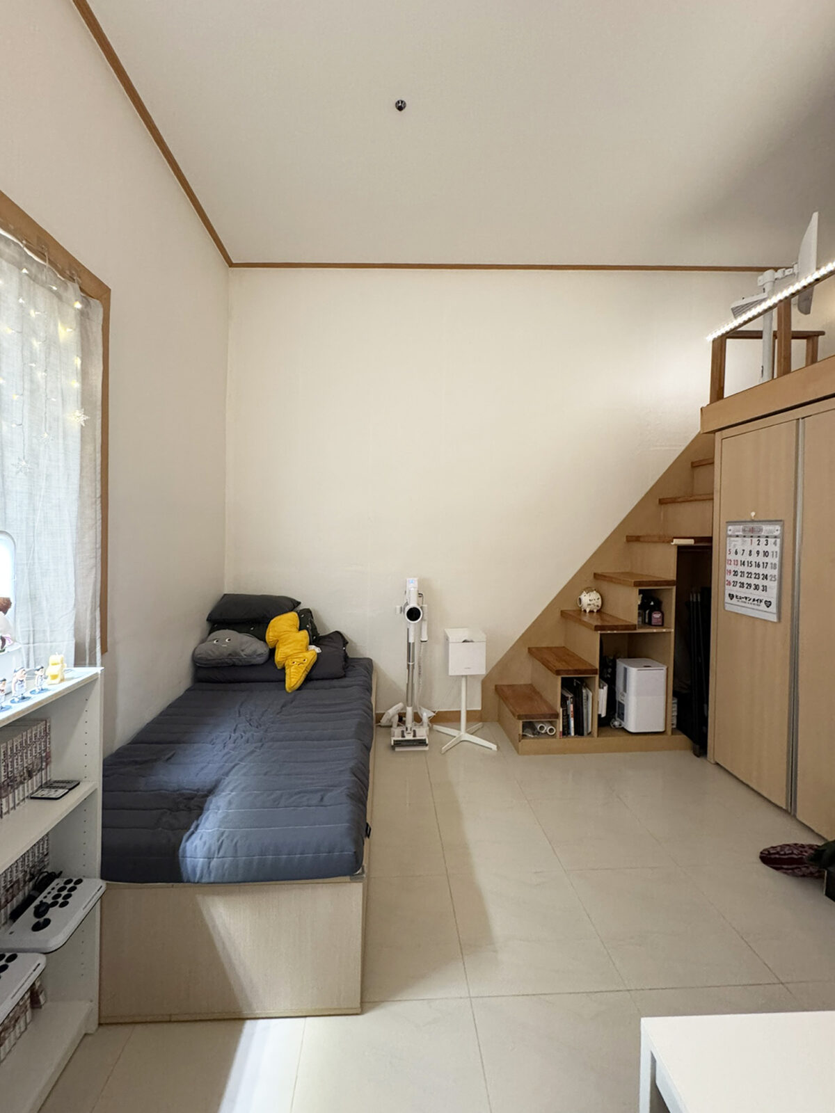 Cozy corner of the Naeson-dong loft with a gray sofa and yellow cushions. Stairs lead to the loft bedroom, and the under-stair area is used for storage.
